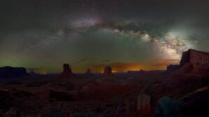 Vía Láctea sobre el desierto de Monument Valley con formaciones rocosas al atardecer y cielo estrellado nocturno.