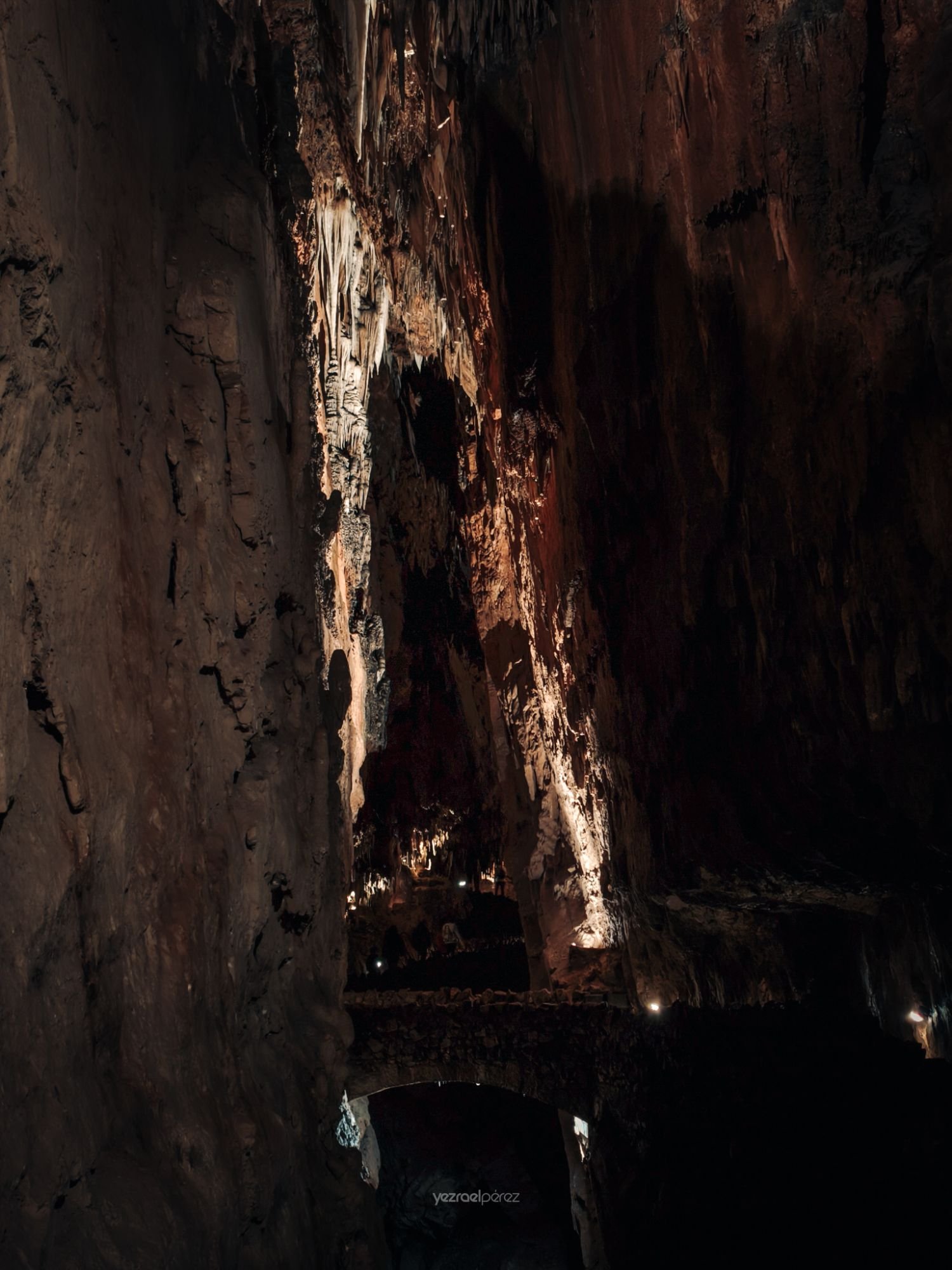 Interior de cueva subterránea iluminada con paredes de roca erosionada, luz natural cenital y pequeños puntos de luz artificial en la base.