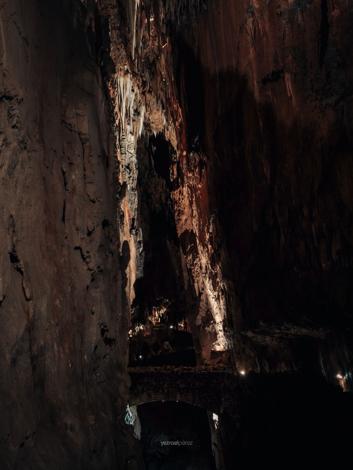 Callejón estrecho de noche con paredes de piedra erosionadas, iluminación lateral que destaca texturas y un vehículo en la penumbra al fondo