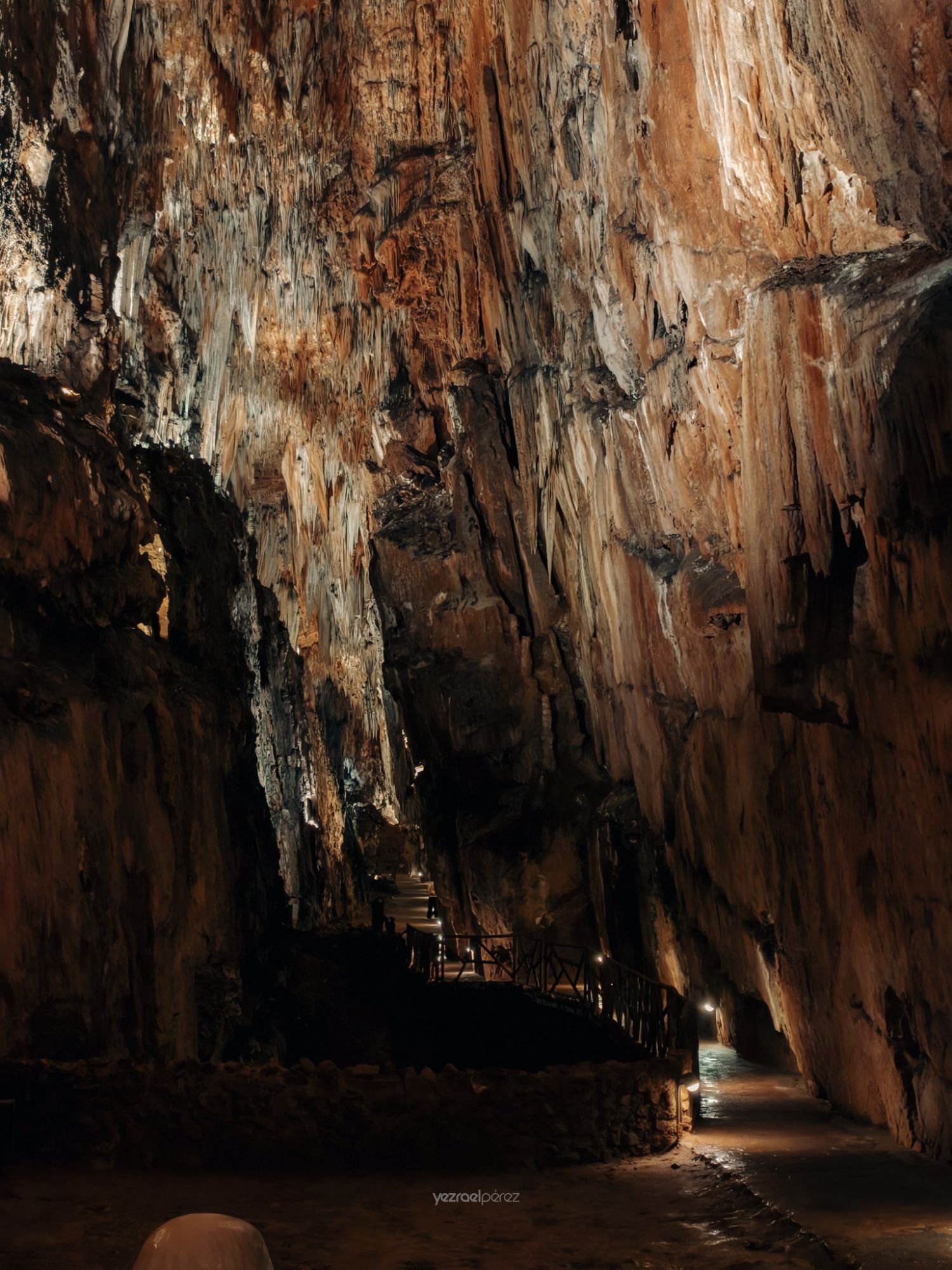 Estrecho cañón de roca con paredes erosionadas en tonos ocres y blancos, iluminado artificialmente con escaleras y pasarela de madera en el interior